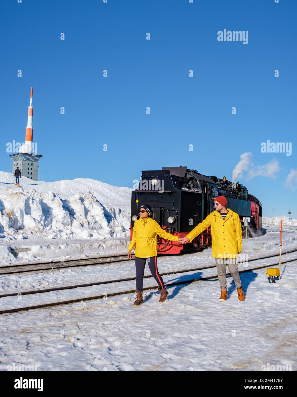 Un paio di uomini e donne che guardano il treno a vapore durante l'inverno nella neve nel parco nazionale di Harz Germania, treno a vapore Brocken Bahn sulla strada attraverso il paesaggio invernale Foto Stock