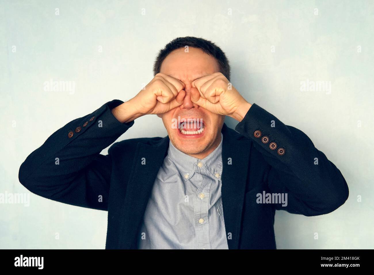 Ritratto di un giovane uomo d'affari che piange. un uomo grida come un bambino. ragazzo in tuta urla con la bocca spalancata. Psico lavoratore. Foto Stock