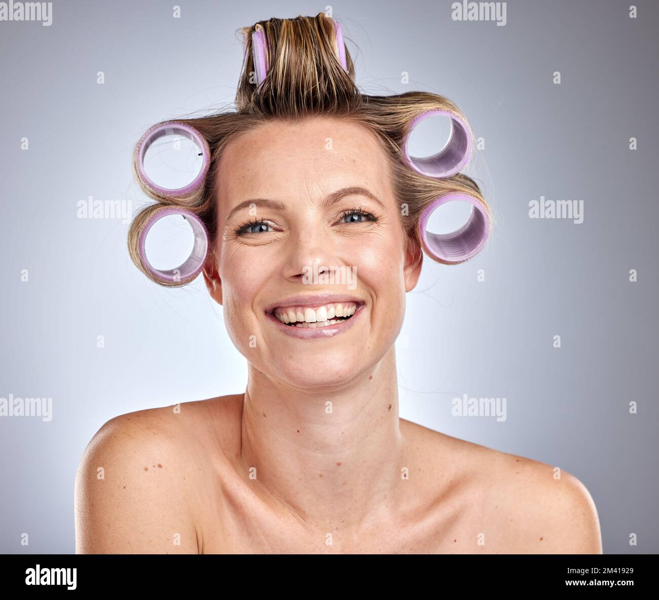 Cura dei capelli, styling e donna con un set di rulli, manutenzione di bellezza e felice contro uno sfondo grigio studio. Parrucchiere, preparazione e ritratto del viso Foto Stock