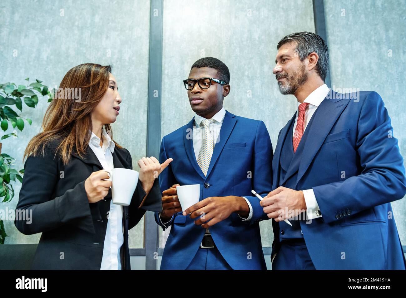 Angolo basso di imprenditore asiatico femminile in abbigliamento formale con tazza di bevanda calda gesticulating e parlare con diversi colleghi maschi durante la brea caffè Foto Stock