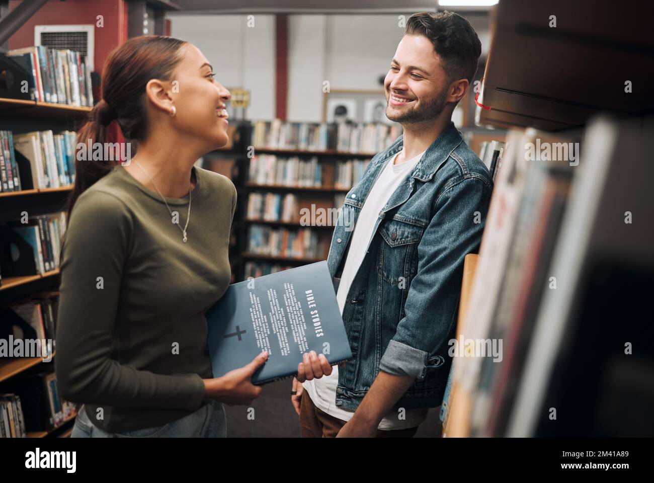 Uomo, donna e parlare in biblioteca, conoscenza e legame con il sorriso. Giovani donne, uomini e studenti in libreria, istruzione e libro per l'apprendimento Foto Stock