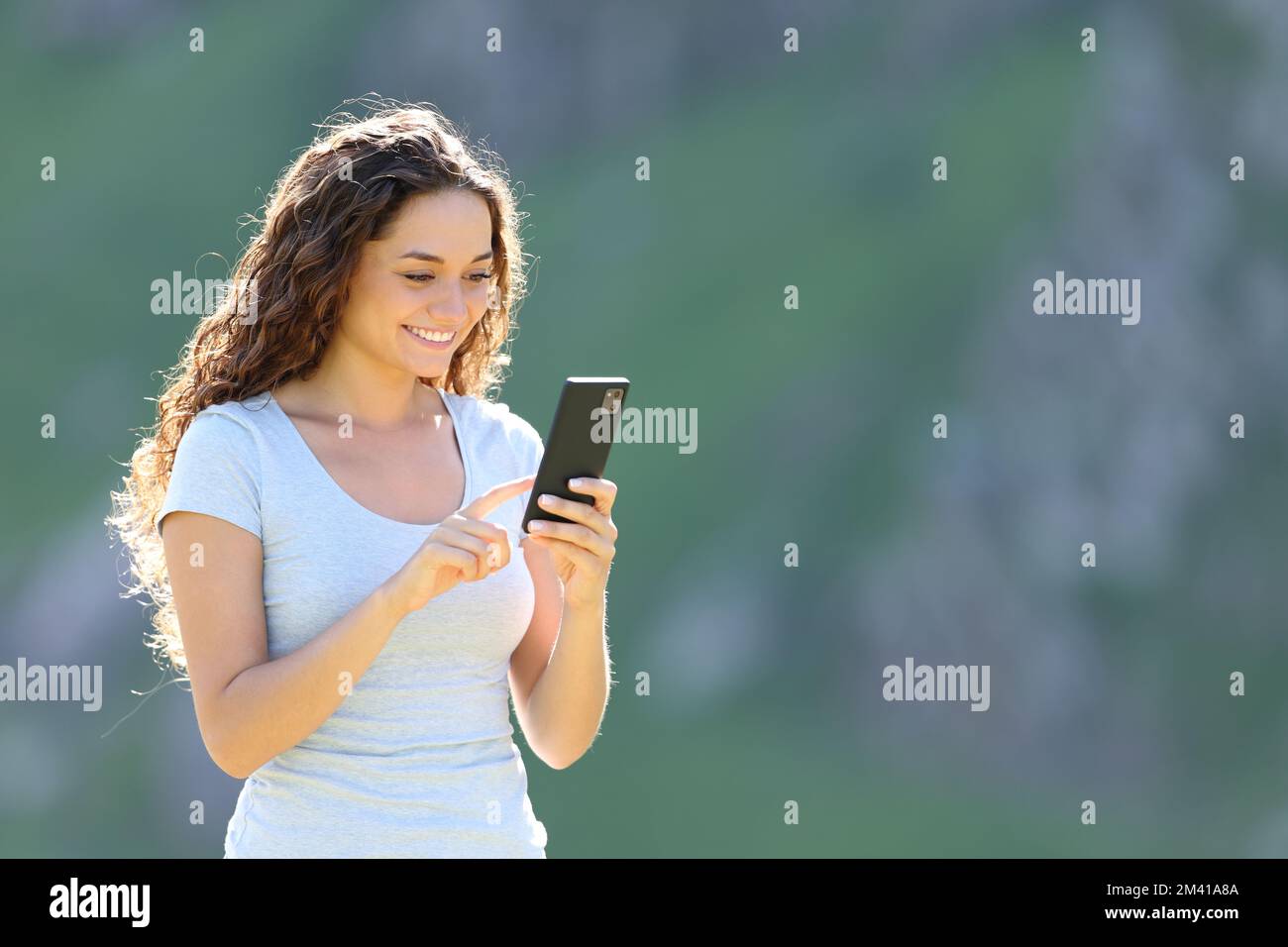 Donna felice in piedi in montagna utilizzando il cellulare Foto Stock
