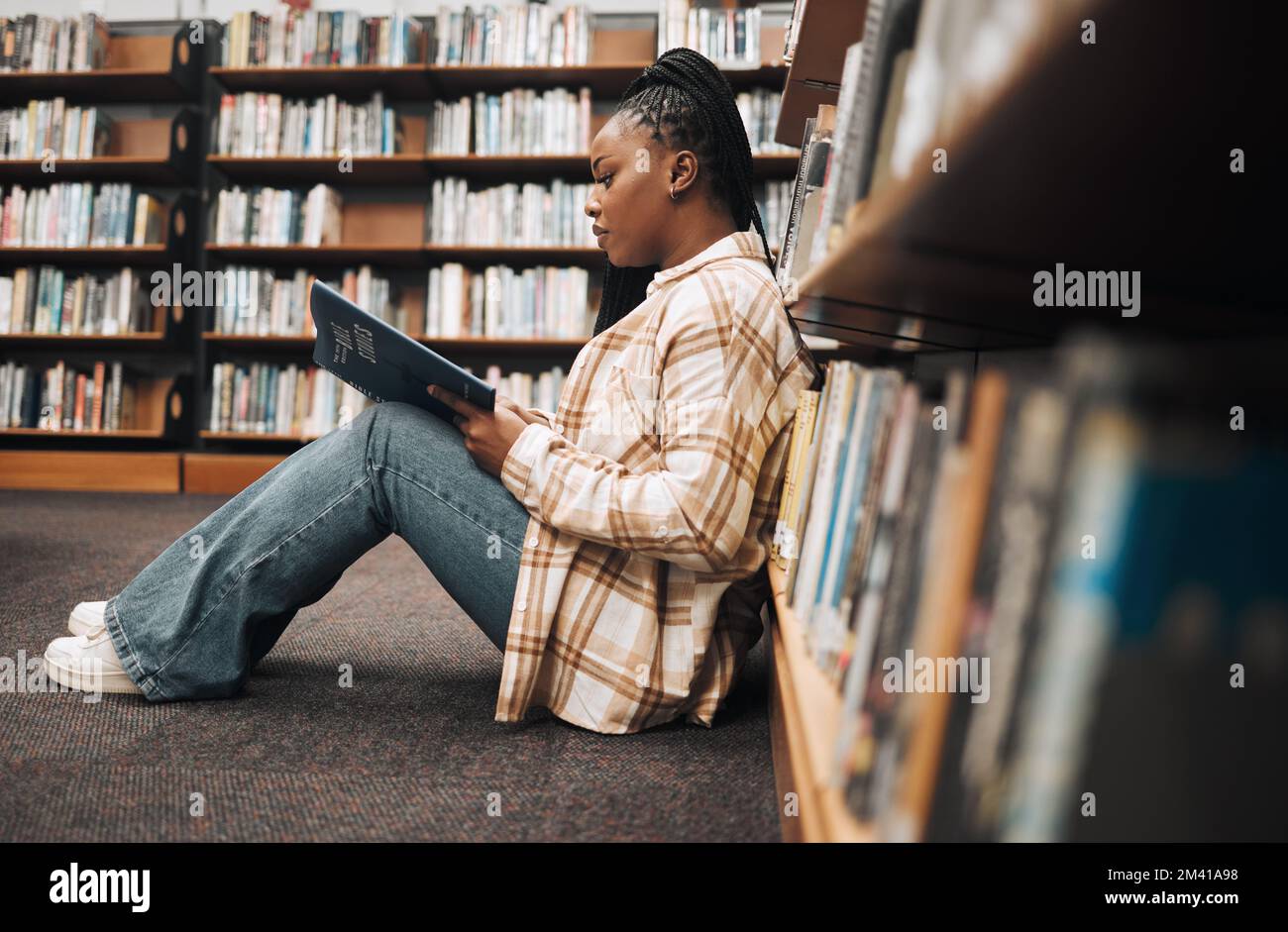 Biblioteca, studente universitario e donna nera che leggono libri al piano terra per l'istruzione, lo studio e l'apprendimento del campus. Studente universitario, ragazza e. Foto Stock