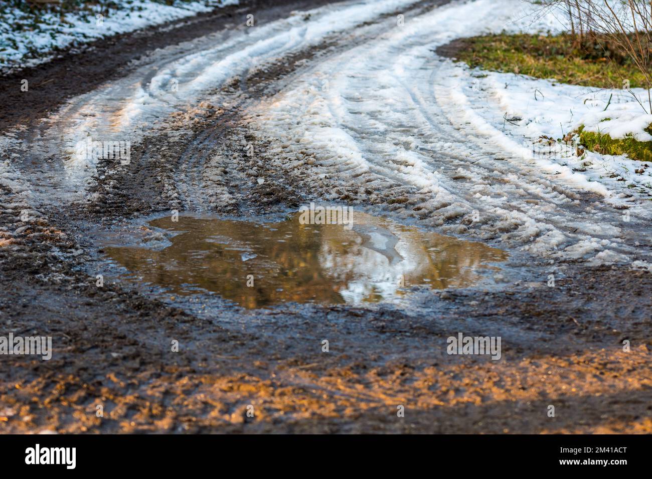 Piccola pozza sulla strada, riflesso in acqua vicino al prato. Neve e inverno Foto Stock