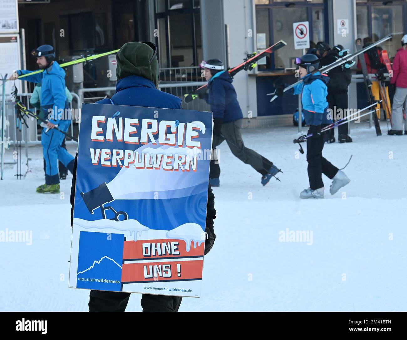 Garmisch Partenkirchen, Germania. 18th Dec, 2022. Un membro dell'organizzazione di conservazione Mountain Wilderness protesta con un poster presso la stazione a valle del Hausbergbahn nel comprensorio sciistico Garmisch Classic. Con la loro azione, vogliono attirare l'attenzione sulla questione dello spreco di energia e acqua attraverso cannoni da neve. Credit: Angelika Warmuth/dpa/Alamy Live News Foto Stock