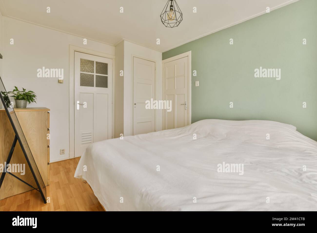 una camera da letto con pareti verdi e letti bianchi, pavimento in legno e una porta aperta che conduce ad un'altra stanza Foto Stock
