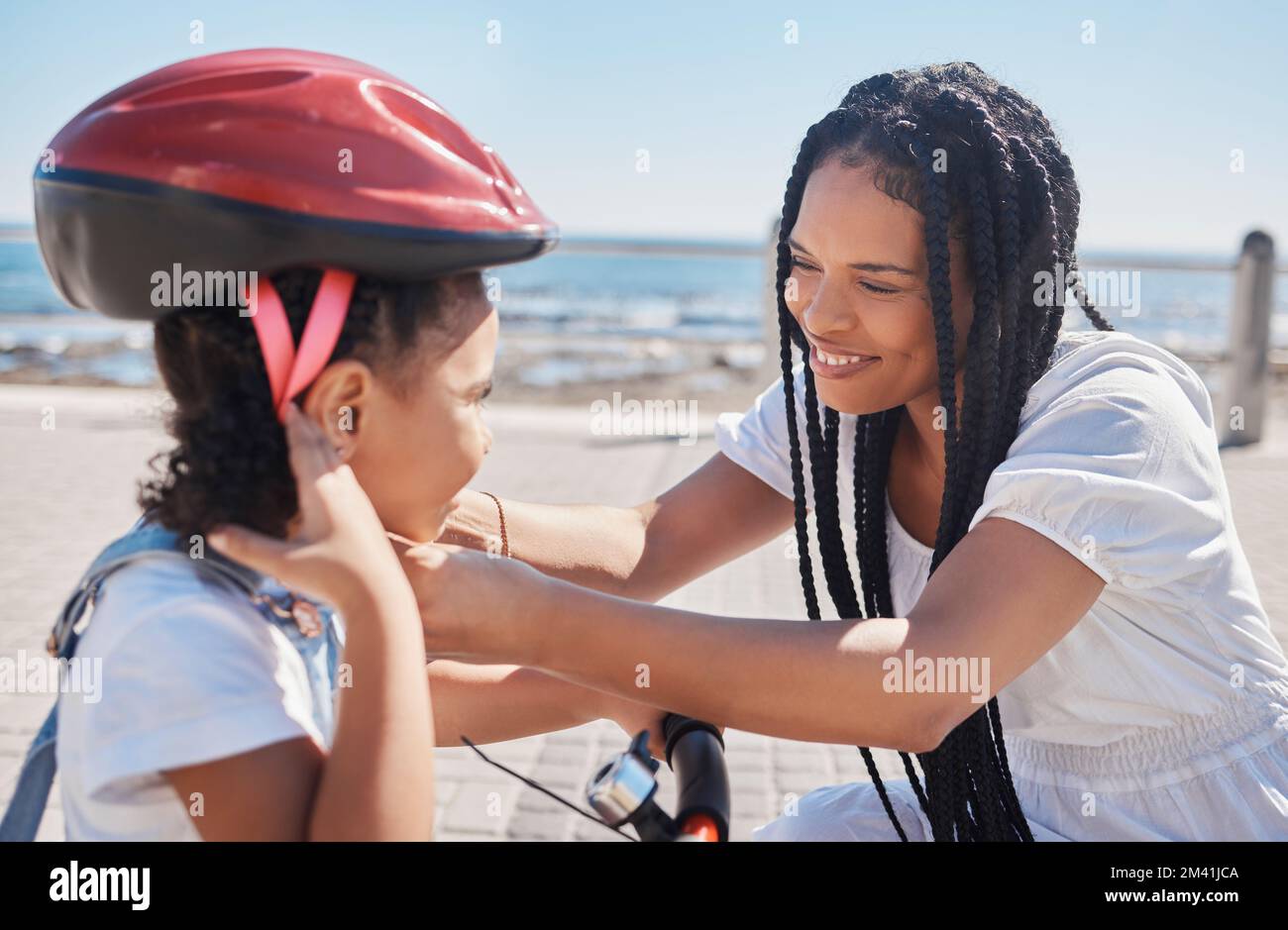 Madre, bambino o bicicletta casco aiutare in spiaggia, città oceano o mare in sicurezza di equitazione, apprendimento di sicurezza o attività di divertimento protezione. Sorriso felice, mom di legame Foto Stock