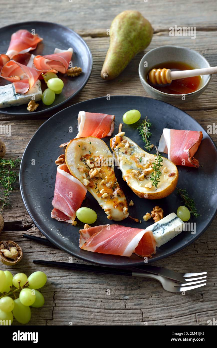 Pere al forno farcite con formaggio gorgonzola, servite con noci e pancetta altoatesina Foto Stock