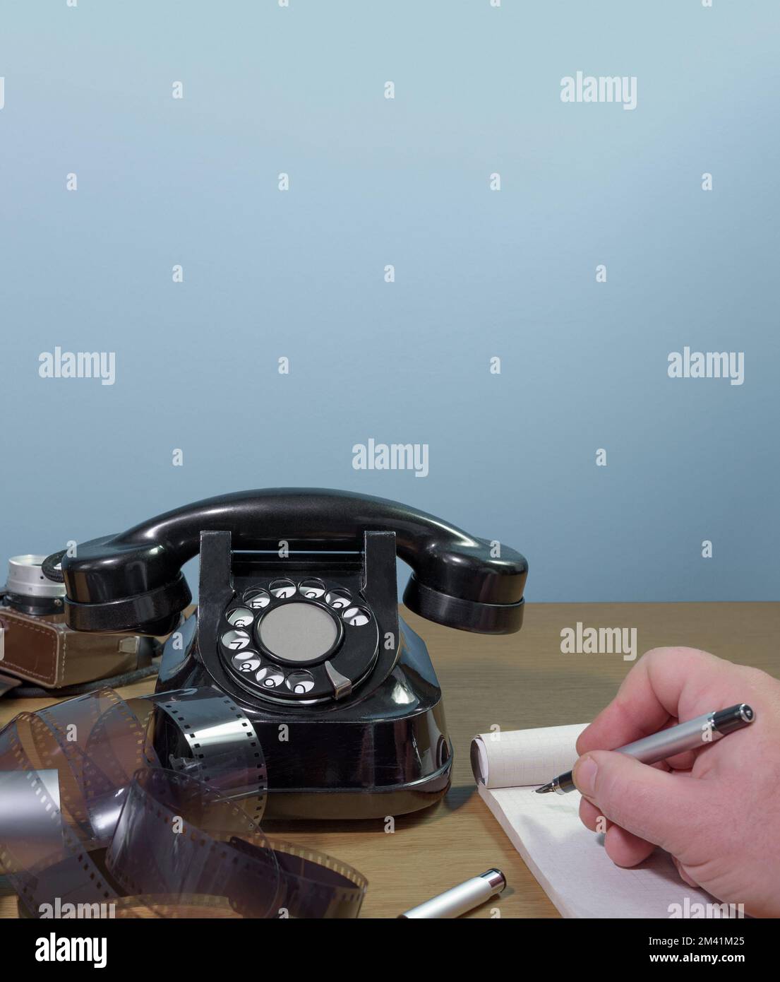 La mano dell'uomo scrive in un taccuino con una penna stilografica. Vecchio telefono, vecchia macchina fotografica e film su un tavolo di legno Foto Stock