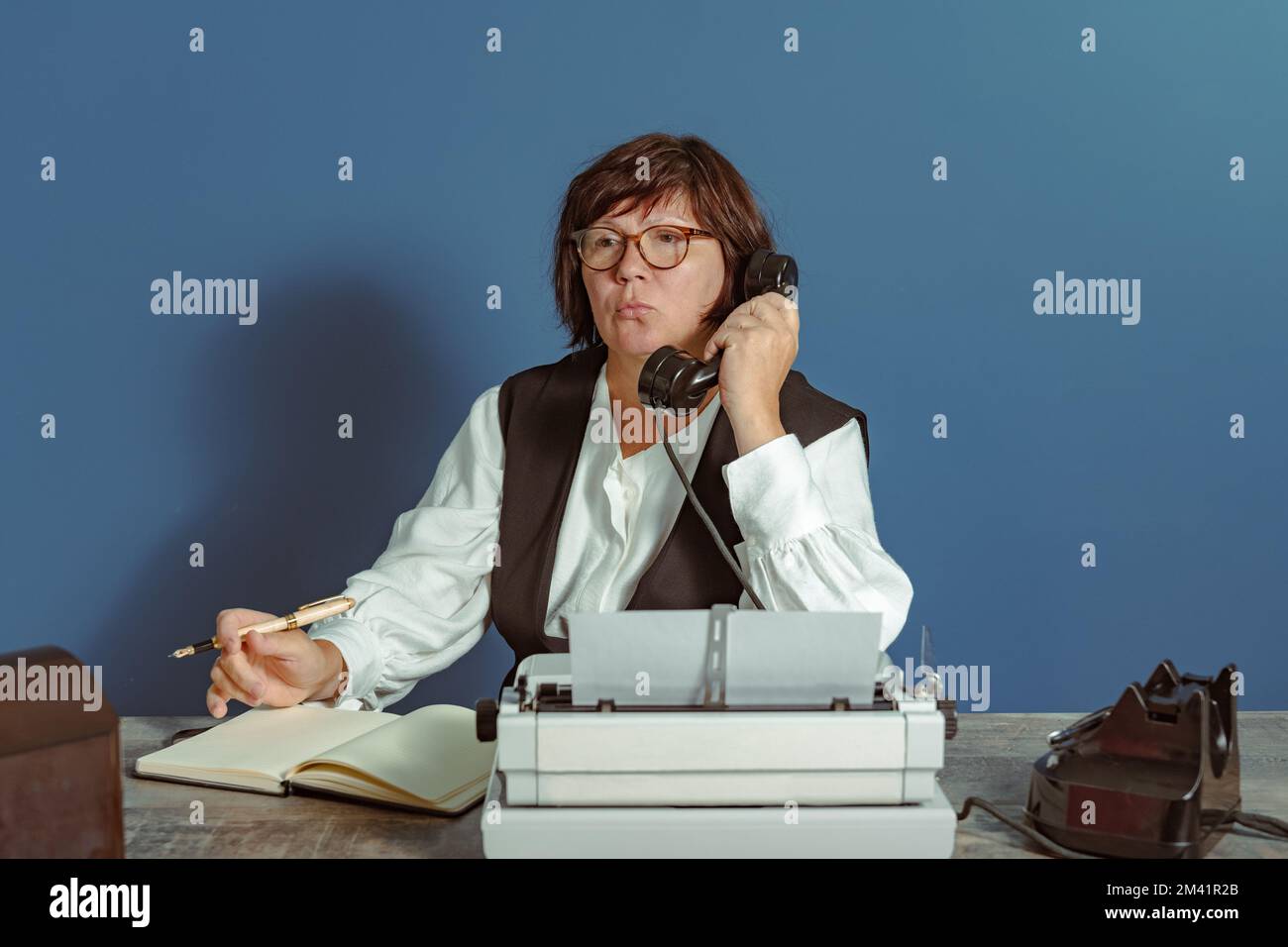 Segretario donna del passato al lavoro. Tavolo con telefono e macchina da scrivere. Vintage. Foto Stock