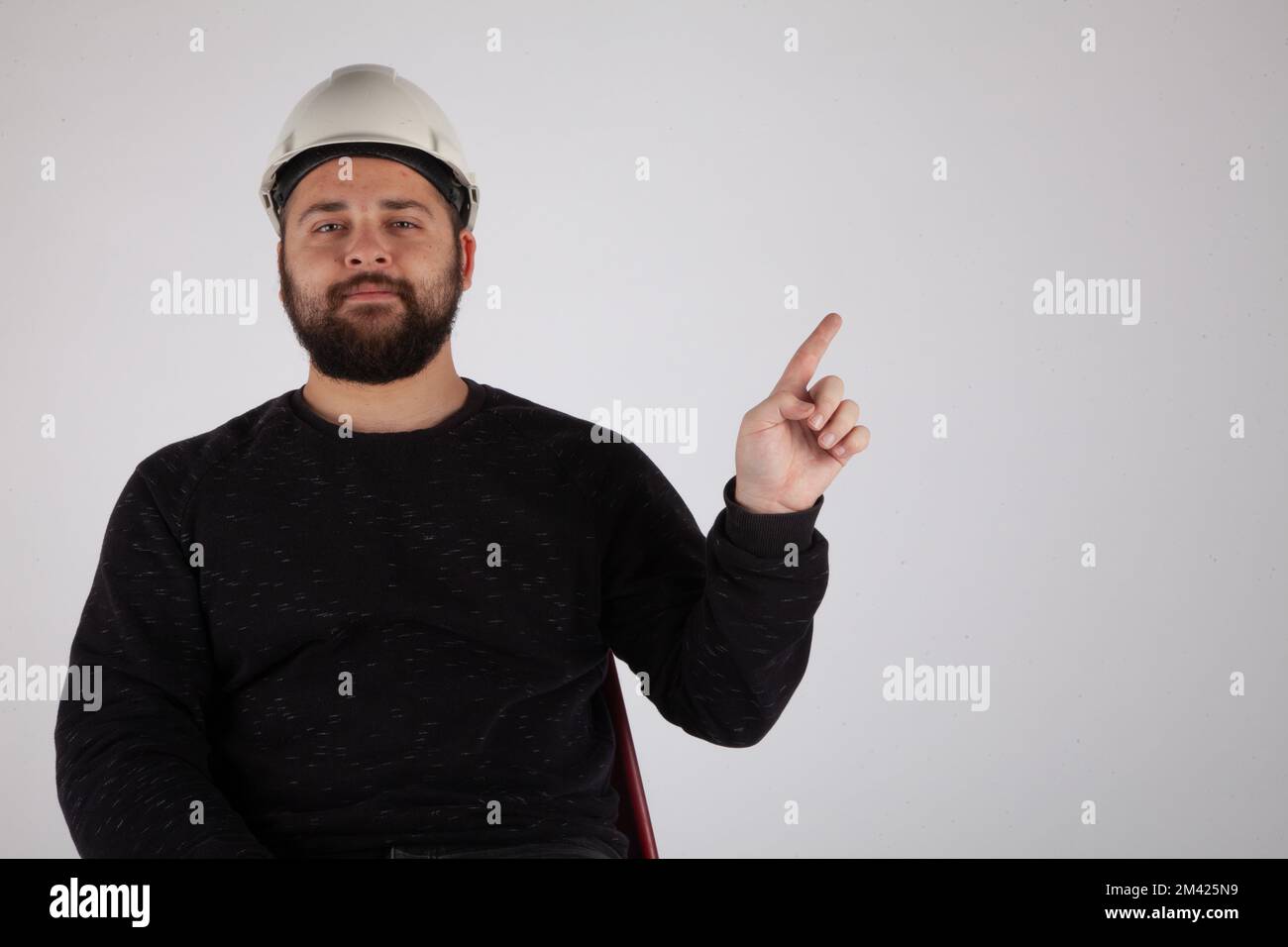 Uomo con elmetto di sicurezza bianco rivolto verso l'area di testo vuota su sfondo bianco isolato. Foto Stock