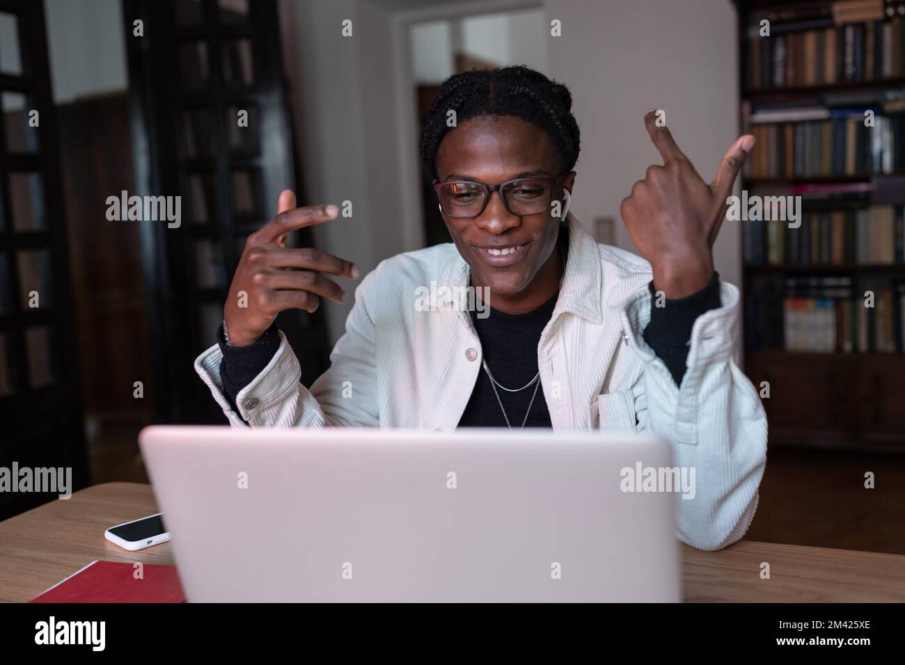 Sorridente giovane uomo africano tutor indossando auricolari wireless parlare con la webcam insegnare online da casa Foto Stock