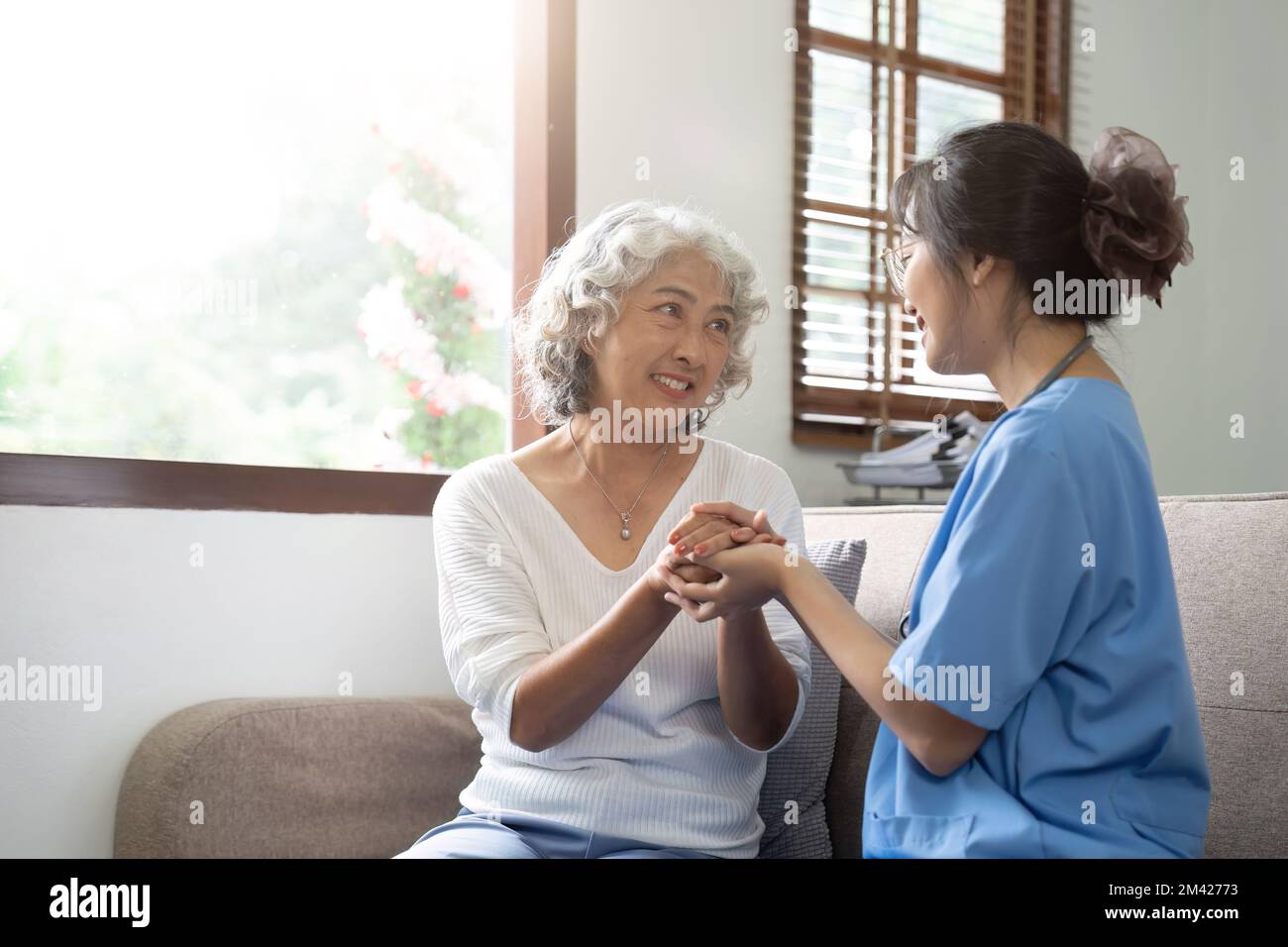 Un paziente felice tiene in mano l'operatore sanitario mentre passa il tempo insieme. Donna anziana in casa di cura e infermiera Foto Stock