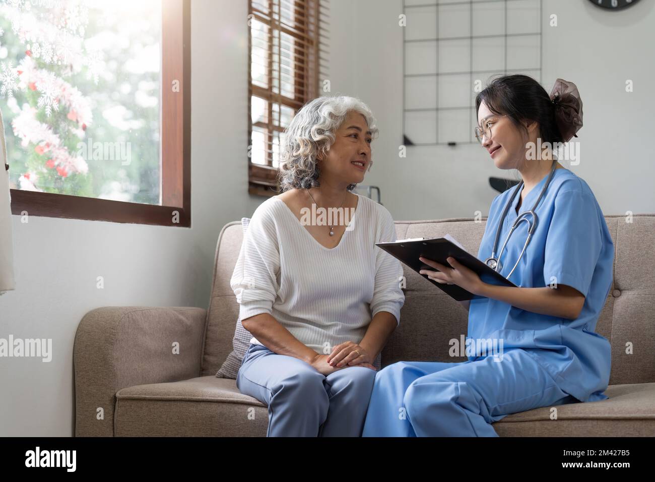 Donna anziana asiatica paziente sul divano con medico donna che indossa la diagnosi stetoscopica Foto Stock