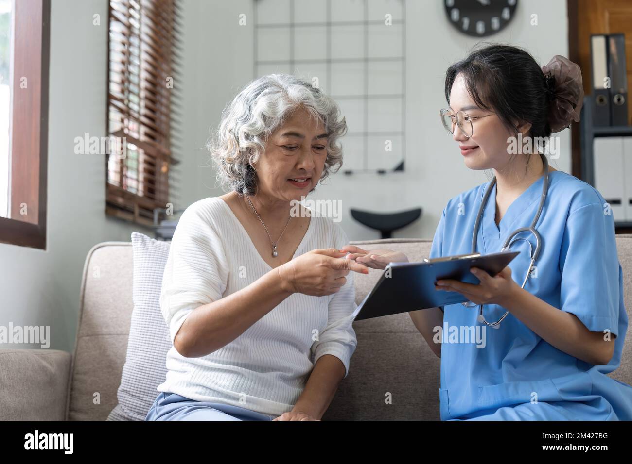 Donna anziana asiatica paziente sul divano che parla con un'infermiera amichevole. concetto di assistenza sanitaria Foto Stock