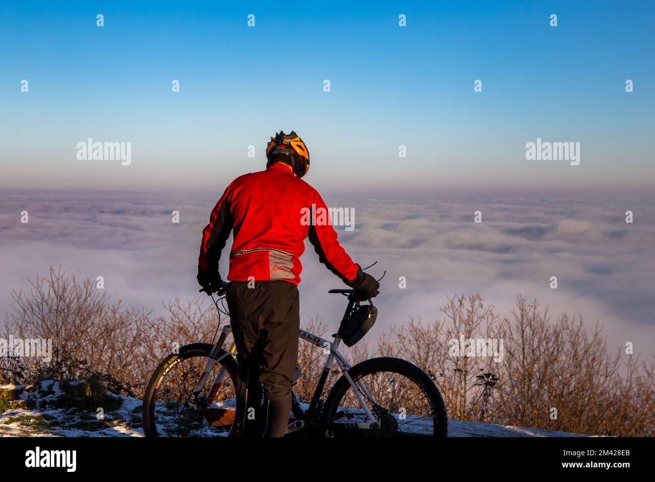 Pausa über den Wolken: Ein Mountainbiker im Pfälzerwald macht Rast an der St.-Anna-Kapelle in Burrweiler. Das tal Liegt im Nebel Foto Stock