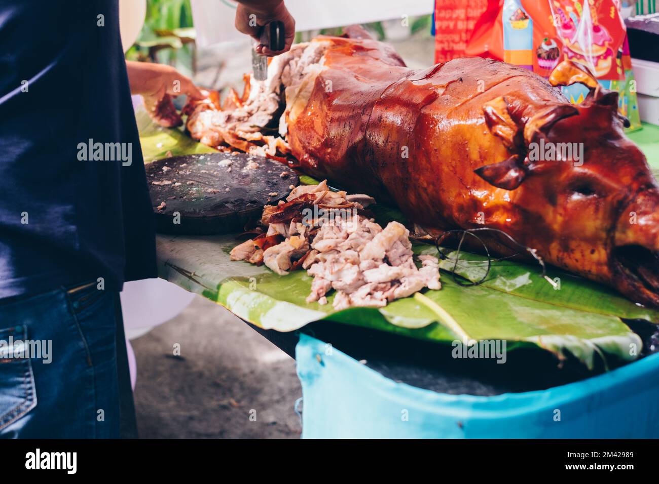 Macellaio affettare a pezzi il preferito di tutti i tempi, il popolare delizioso arrosto di maiale intero croccante o Lechon Baboy posato sulla foglia di banana sul tavolo Foto Stock
