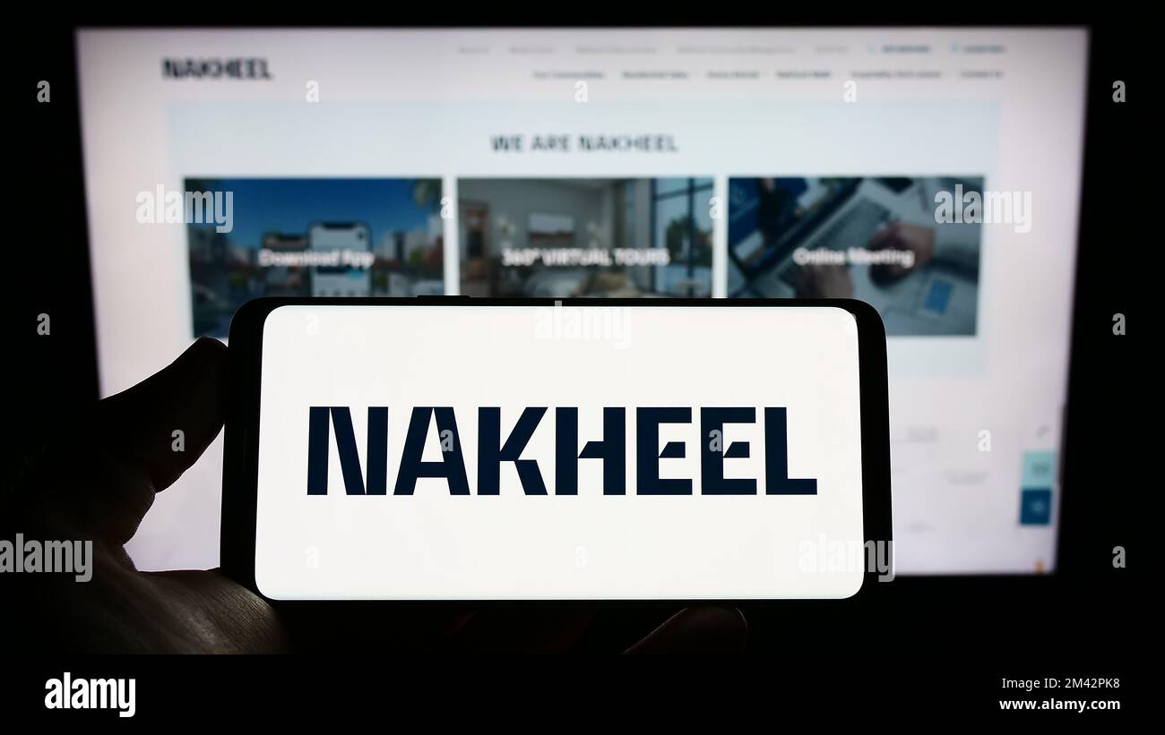 Persona in possesso di smartphone con il logo della società immobiliare Emirati Nakheel Properties sullo schermo di fronte al sito web. Messa a fuoco sul display del telefono. Foto Stock