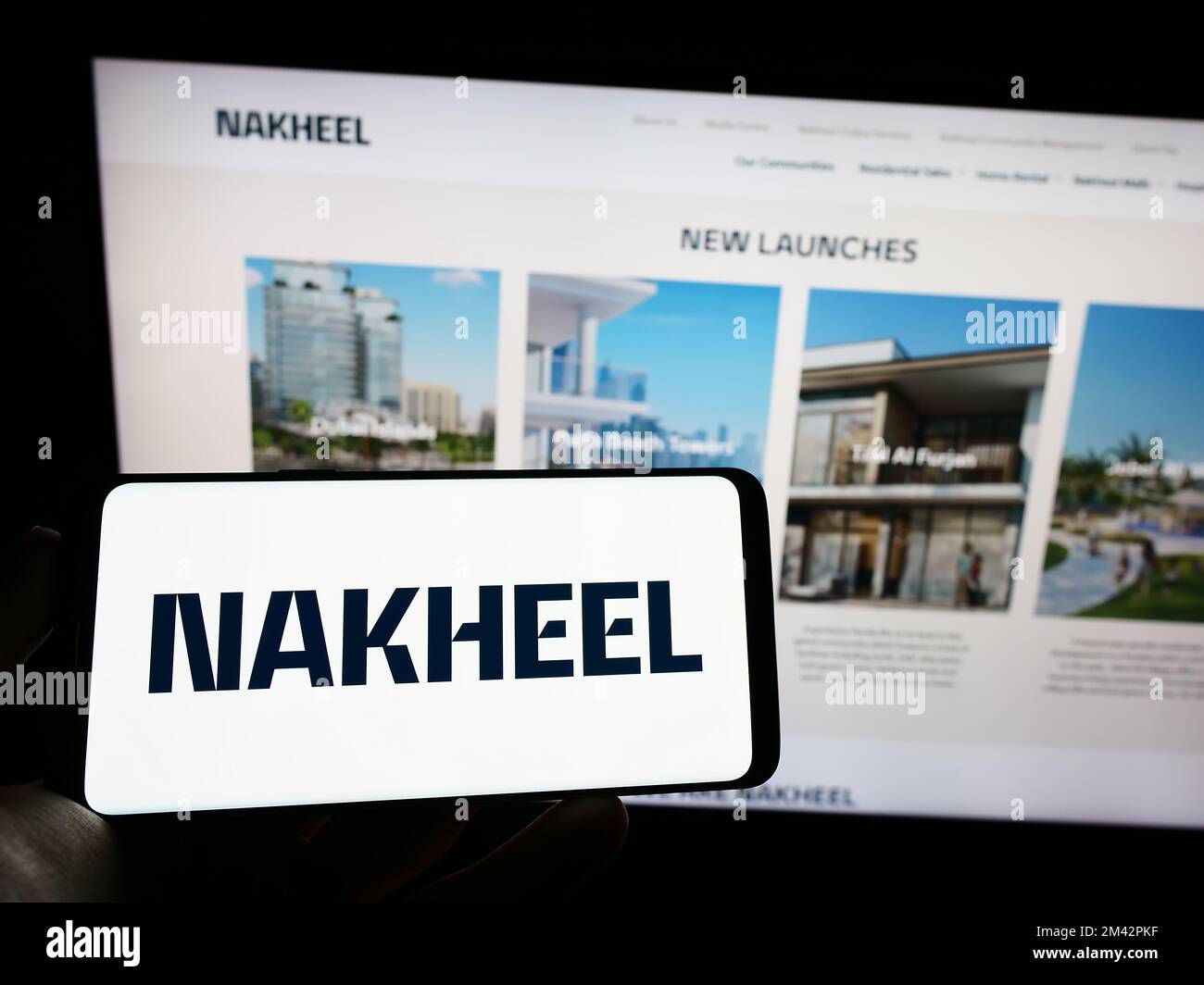 Persona che tiene il telefono mobile con il logo della società immobiliare Emirati Nakheel Proprietà sullo schermo di fronte alla pagina web. Messa a fuoco sul display del telefono. Foto Stock