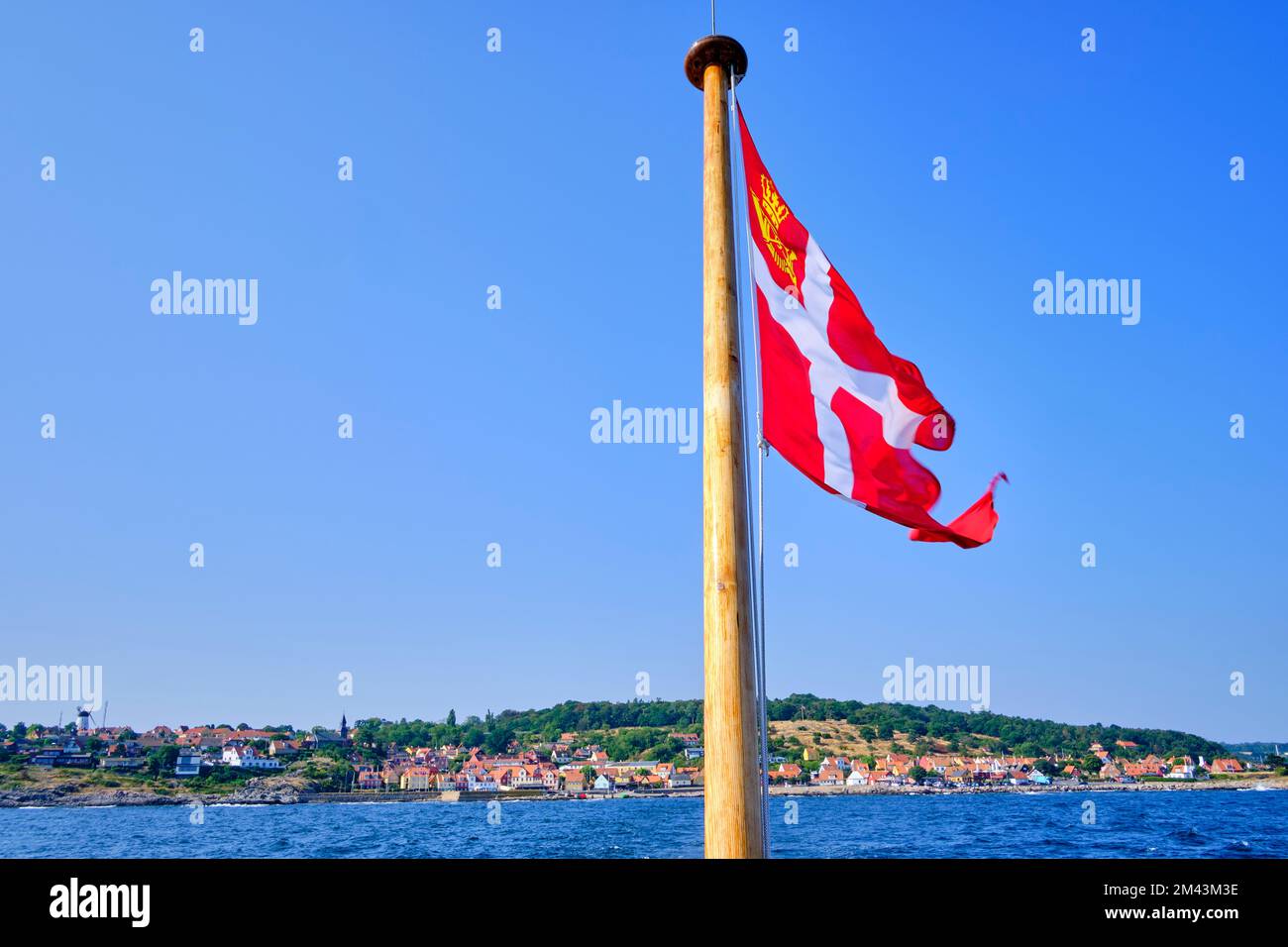Bandiera danese a poppa di una barca da escursione e vista pittoresca della costa di Gudhjem, Bornholm isola, Danimarca. Foto Stock