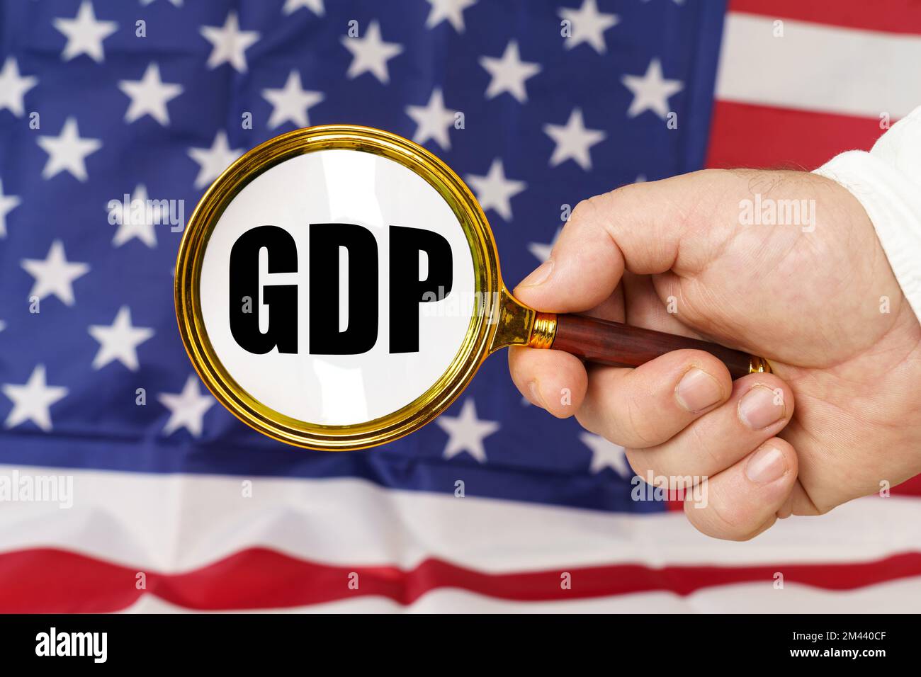 Davanti alla bandiera americana, un uomo tiene in mano una lente d'ingrandimento con l'iscrizione - GDP. Foto Stock