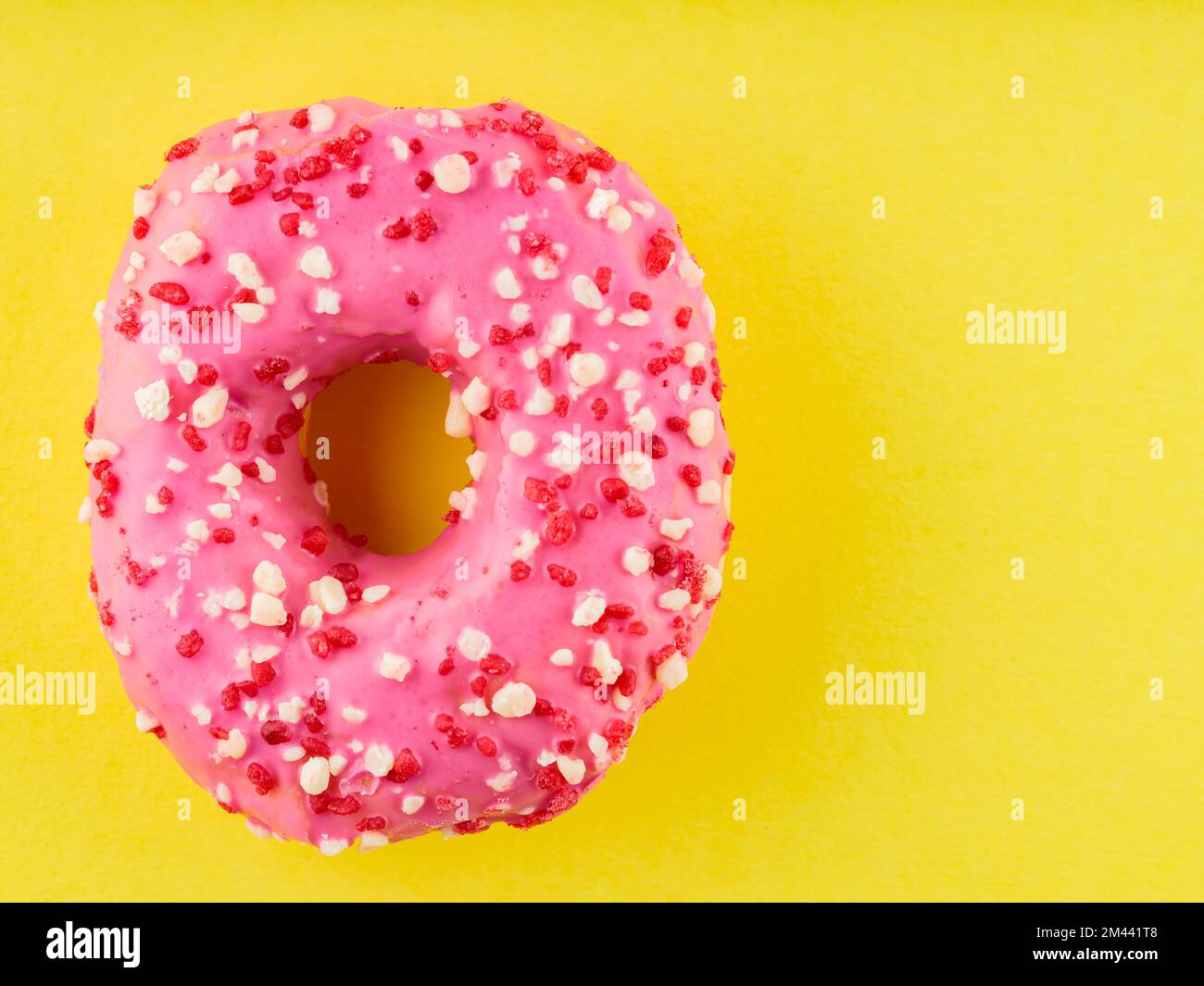 Ciambella rosa dolce con spolverini multicolore su fondo giallo. Dessert dolce colorato Foto Stock