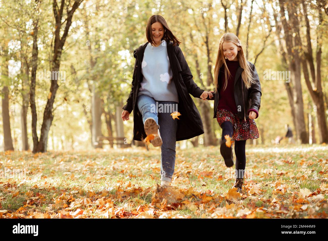 Mischiano, giocoso, felice, sorridente spensierato donna e ragazza giocare e ballare, calci foglie in autunno foresta dorata. Divertendoti Foto Stock