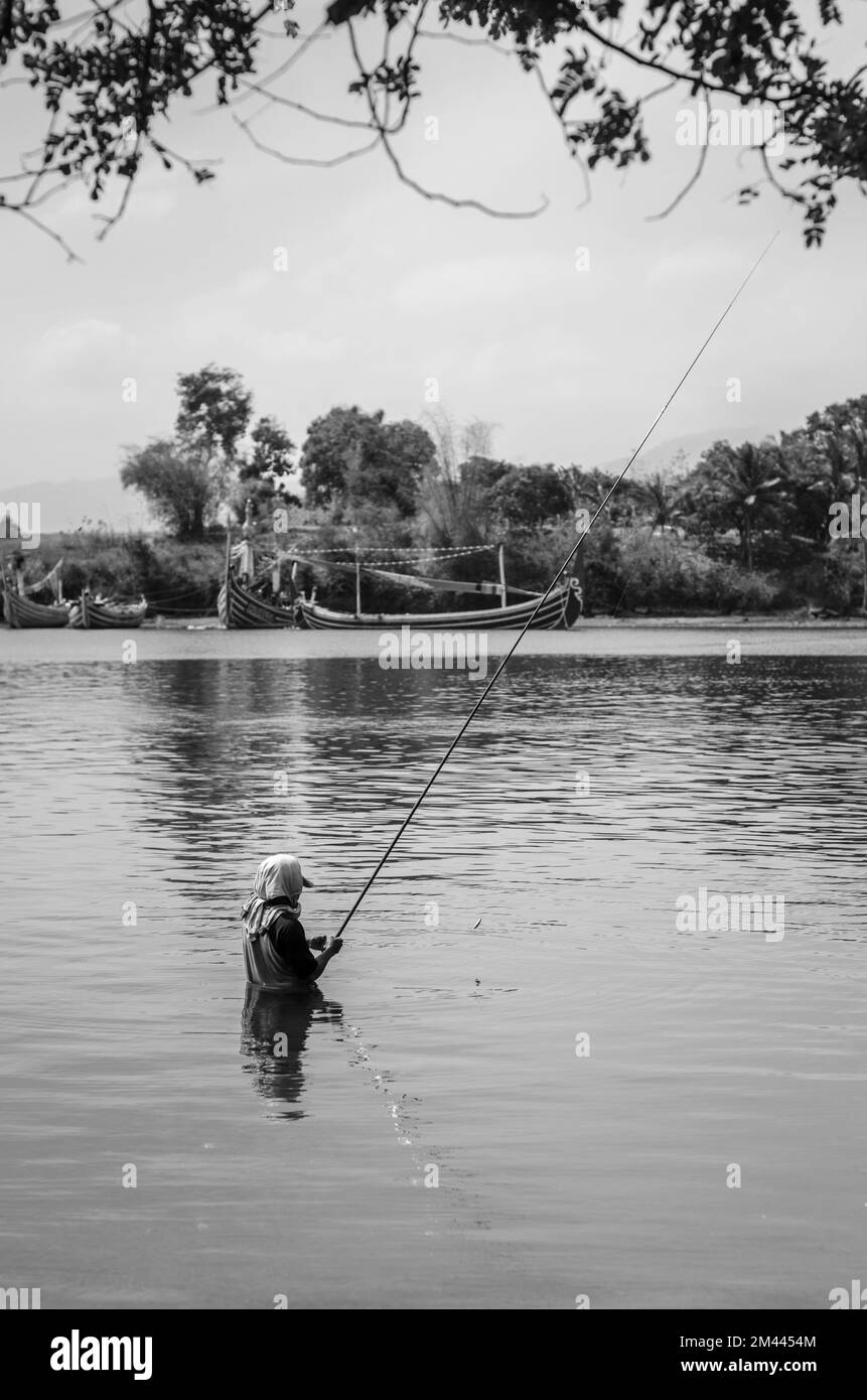 Un colpo in scala di grigi di un uomo che pesca nel lago Foto Stock