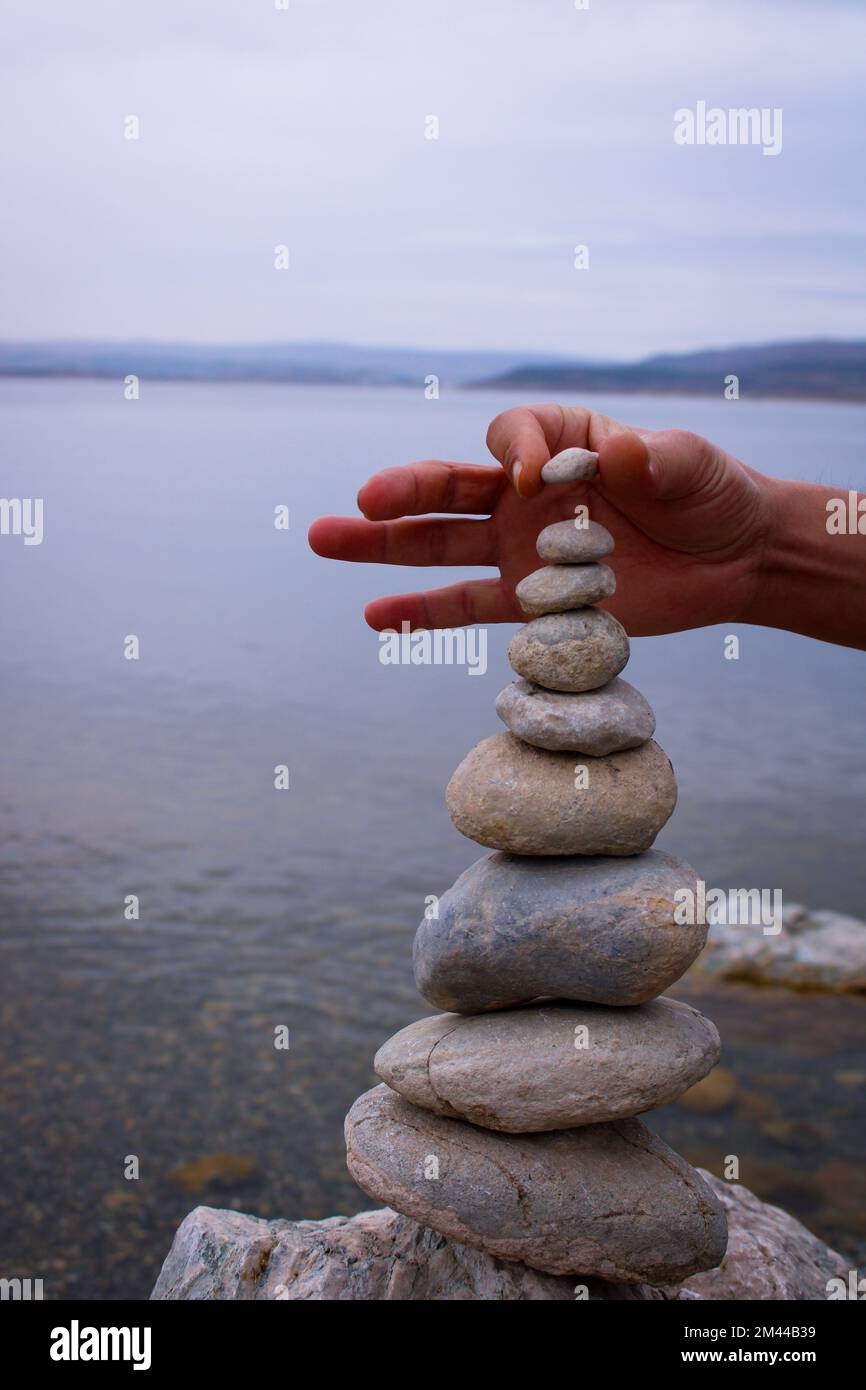 Una mano costruisce l'equilibrio sui ciottoli. Equilibrio perfetto tra la pila di ciottoli sulla riva del mare. Concetto di equilibrio, armonia e meditazione Foto Stock