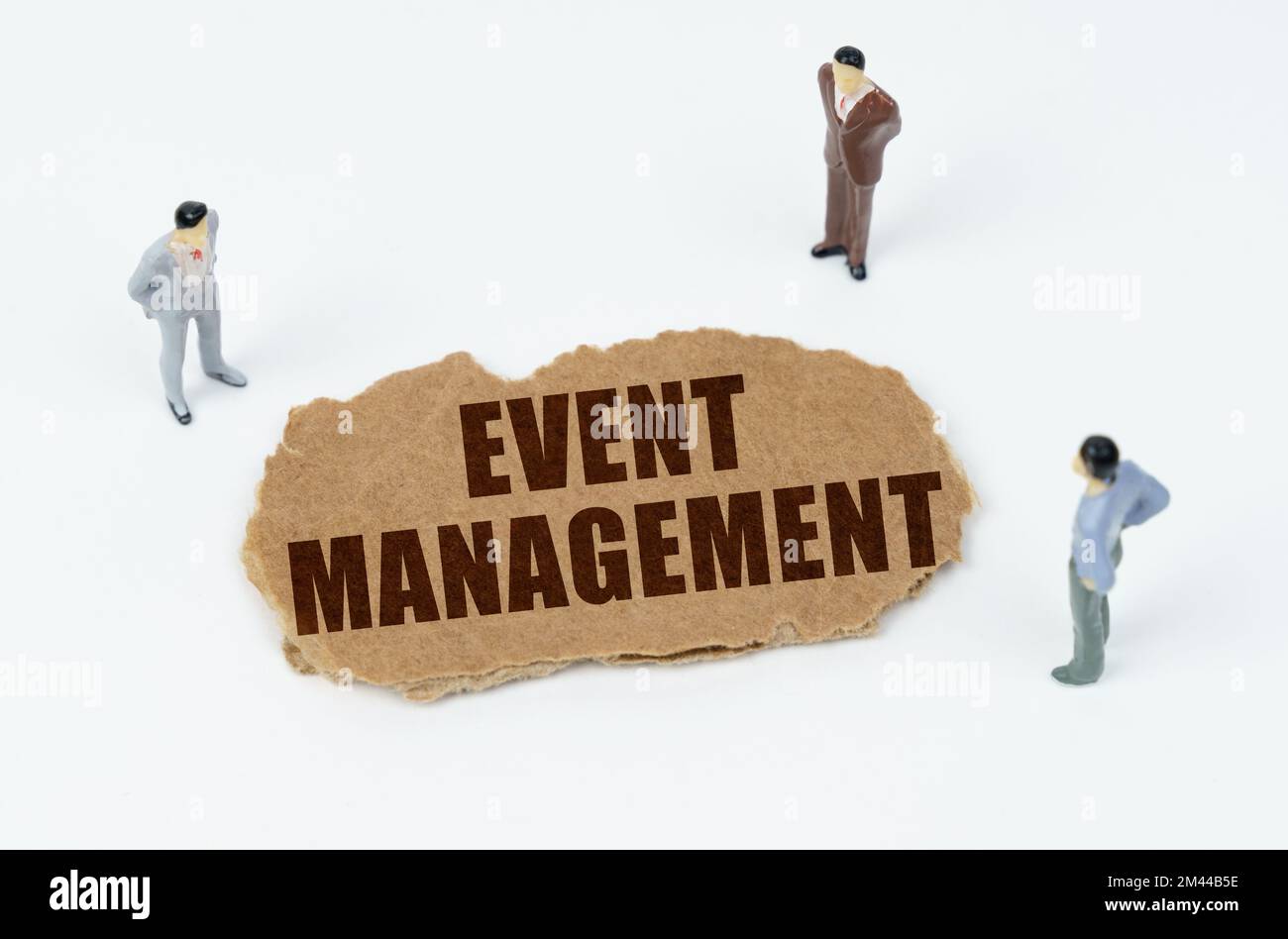 Economia e business concept. Su sfondo bianco, figure di uomini d'affari e cartone strappato con l'iscrizione - GESTIONE EVENTI Foto Stock