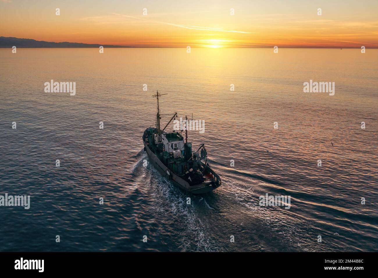 Barca da pesca cattura il pesce al tramonto vista aerea dal drone. Piccola nave da pesca a strascico sulla superficie del mare. Foto Stock
