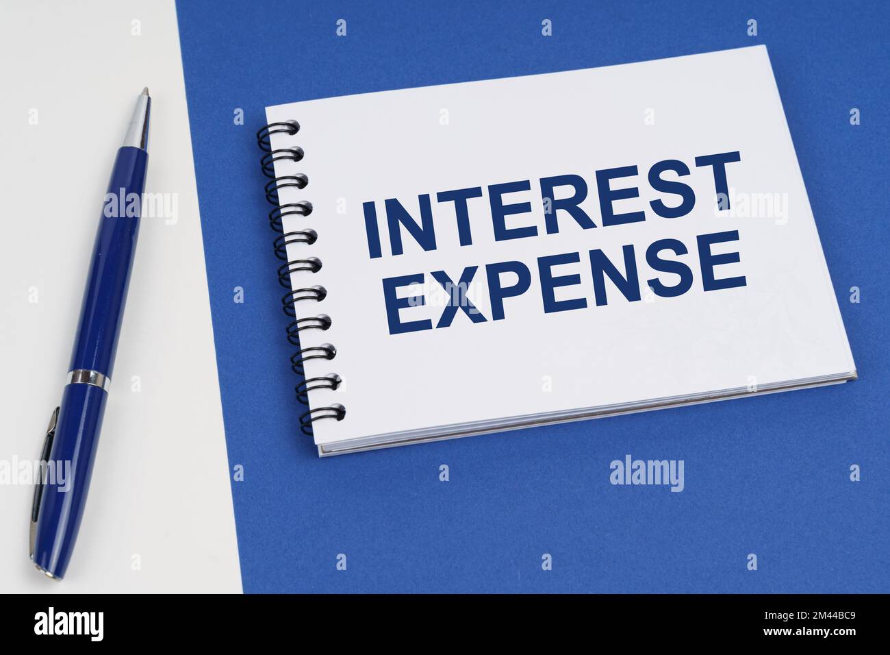 Concetto di business e finanza. Su una superficie blu-bianca si trovano una penna e un notebook con l'iscrizione - spese di interesse Foto Stock