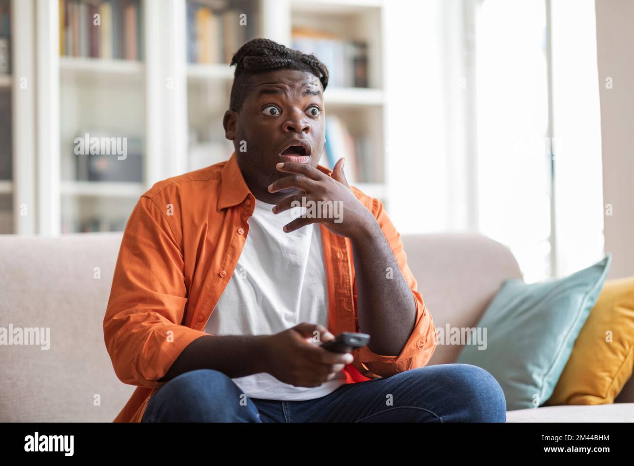 Scioccato afro americano ragazzo seduto a casa, passando la tv Foto Stock