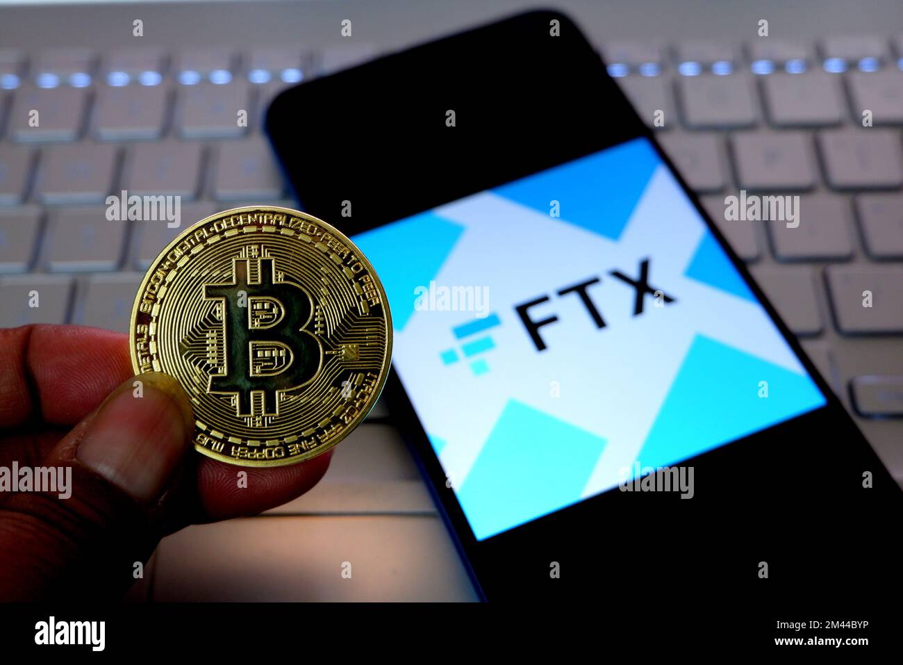 In questa immagine, una moneta di criptovaluta viene visualizzata accanto al logo FTX visualizzato su uno smartphone. Foto Stock