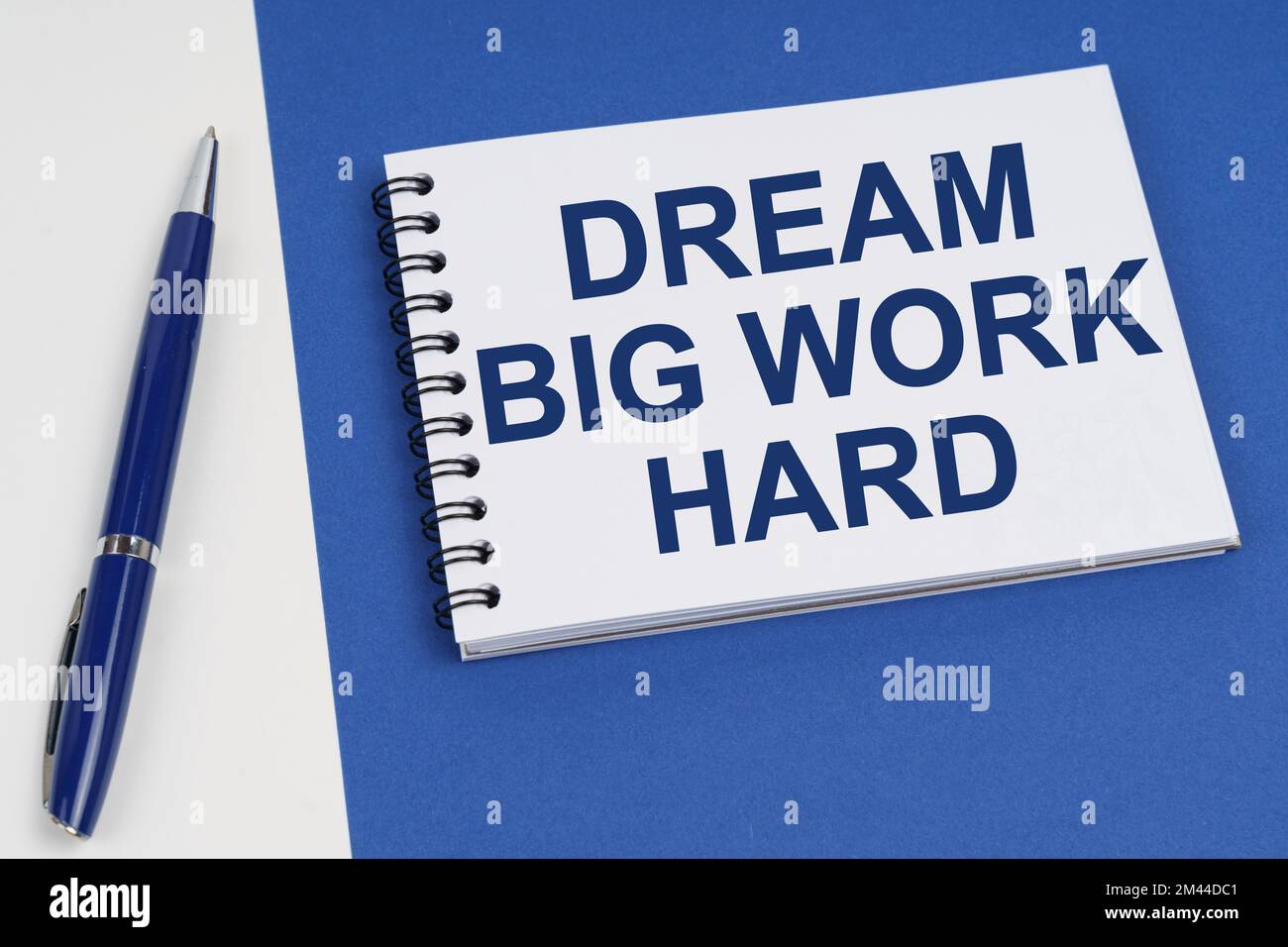 Concetto di business e finanza. Su una superficie blu-bianca si trova una penna e un notebook con l'iscrizione - Dream Big Work Hard Foto Stock