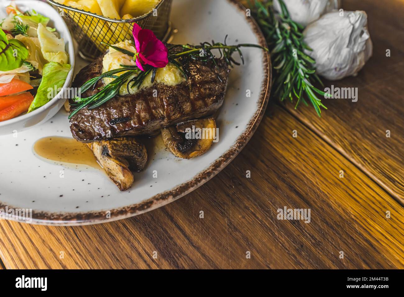 Vista dall'alto di una bistecca di Striploin sui funghi con insalata e patatine fritte sul lato. Piatto con piatto di carne su tavolo di legno. Foto di alta qualità Foto Stock