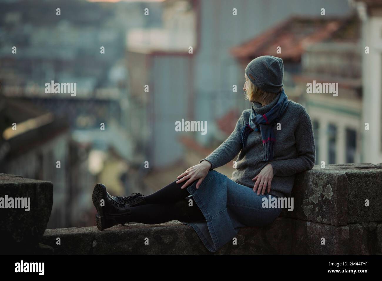 Una donna siede su un antico muro di pietra nel centro di Porto, Portogallo. Foto Stock