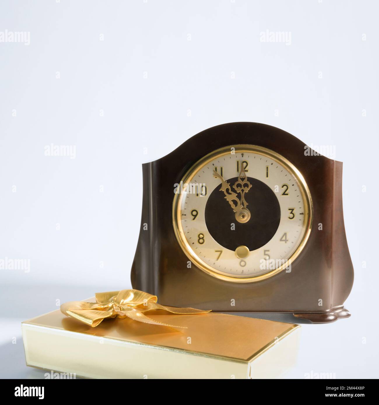 Tempo per i regali. Orologio da tavolo classico e regalo avvolti in arco d'oro. Su sfondo bianco. formato quadrato Foto Stock