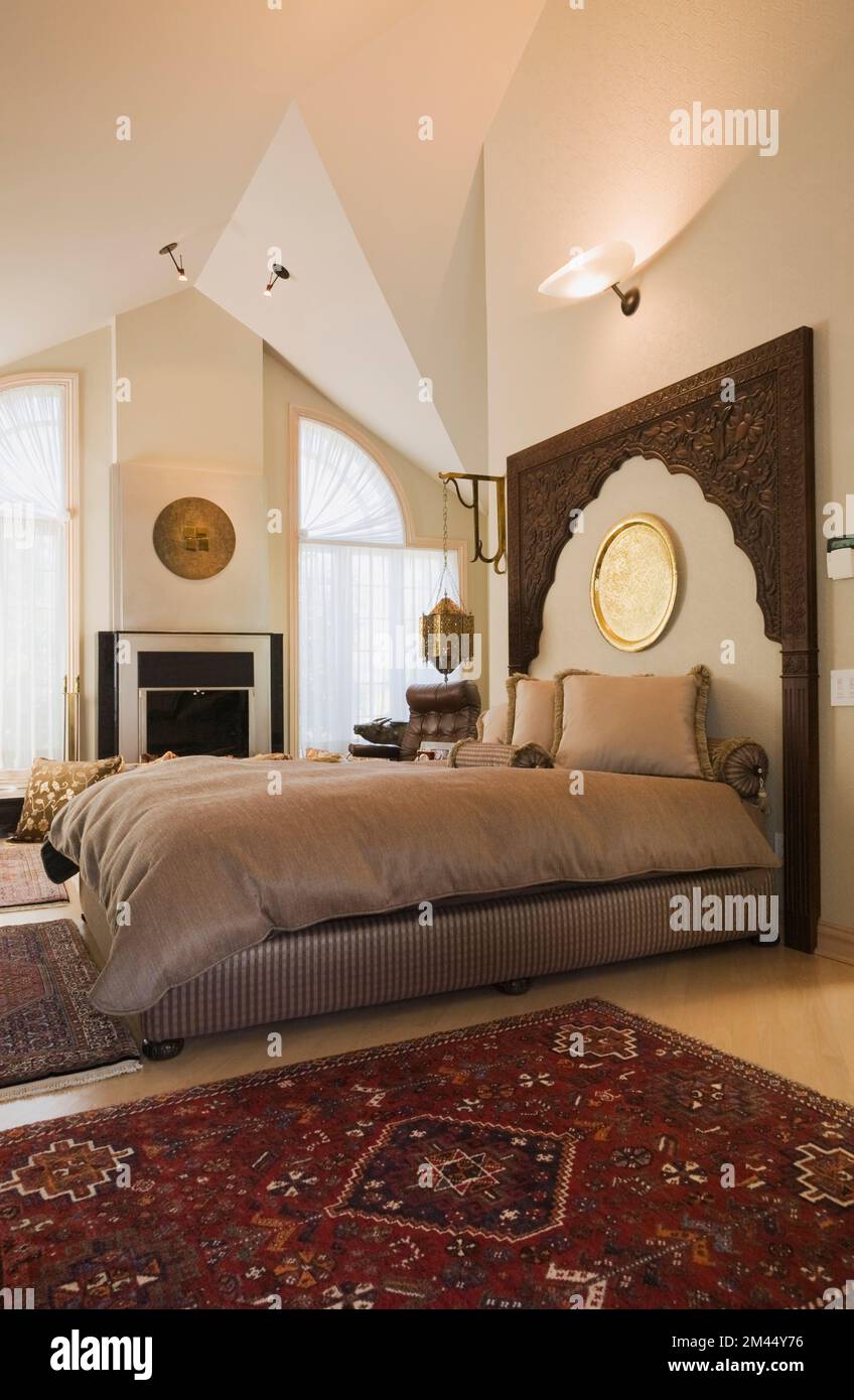Letto queen size con testiera in legno in stile marocchino, camera da letto principale decorata all'interno di una lussuosa casa contemporanea. Foto Stock