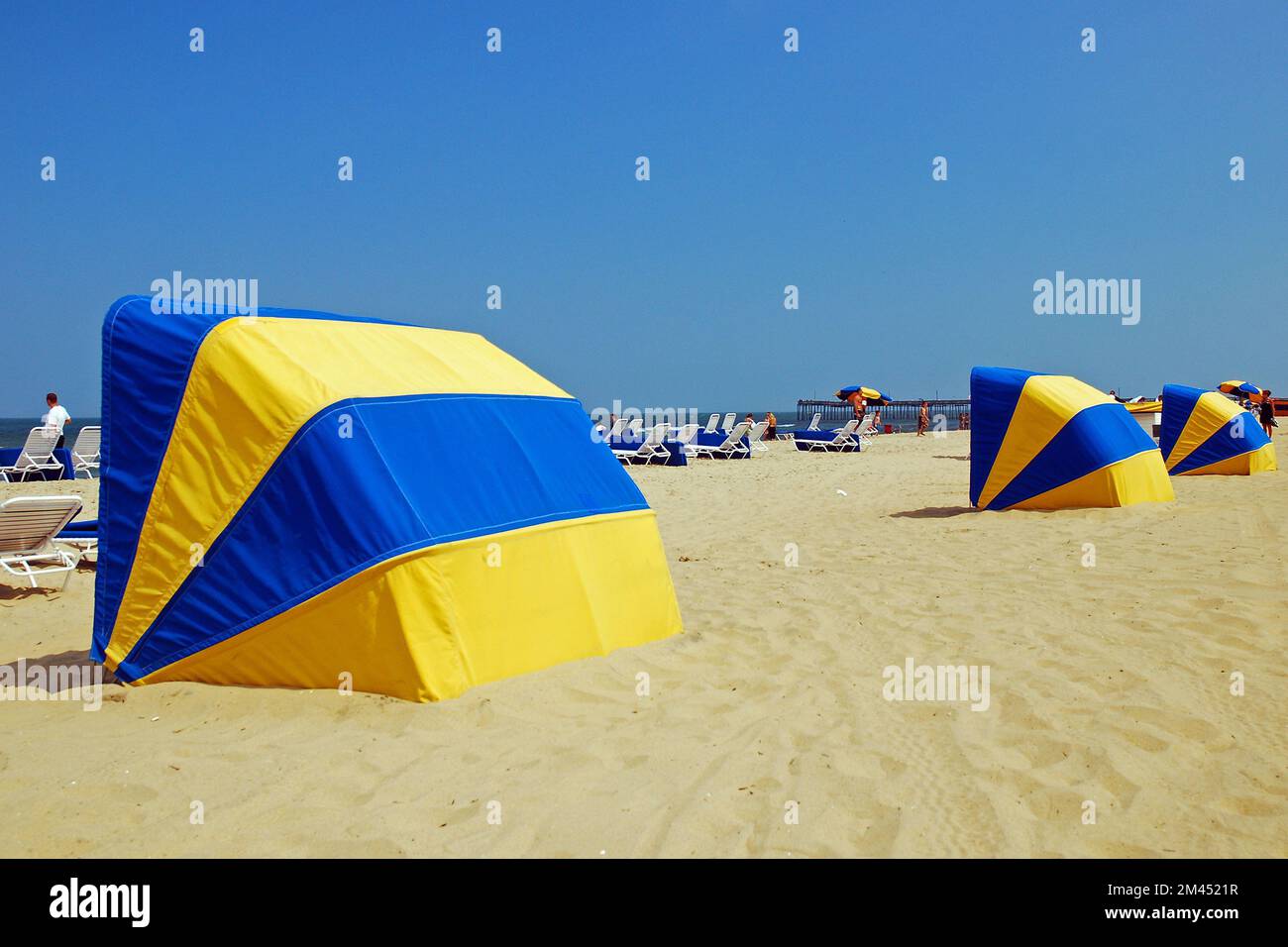 Le capanne di ombrello blu e gialle si allineano lungo Virginia Beach in una giornata di vacanza estiva per proteggere gli amanti della costa dal sole Foto Stock