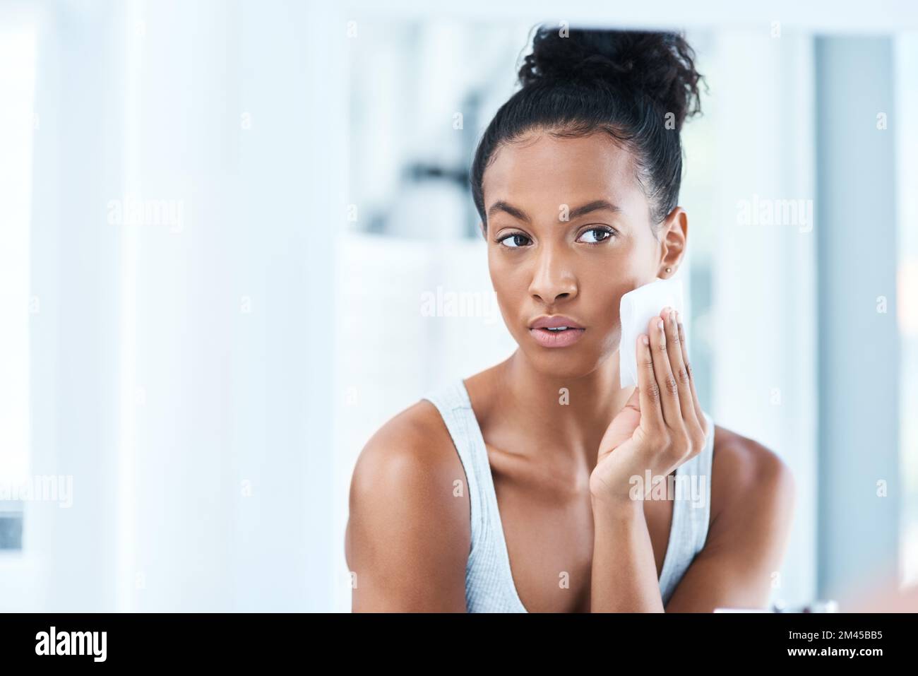 Im che si prende cura della mia pelle, sei tu. Ritratto di una giovane donna attraente che pulisce il viso con un tampone di cotone nel bagno a casa. Foto Stock