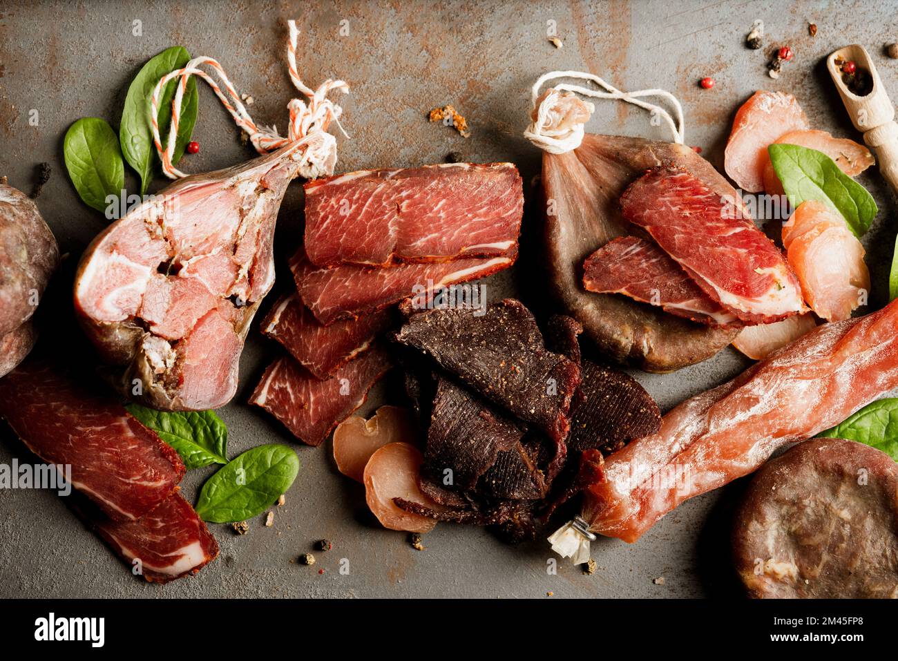 Vari snack di carne affumicata e curata su fondo di tavolo in cemento. Salumi, salsiccia secca, salceson con condimenti - piatto salumi, tradizione Foto Stock