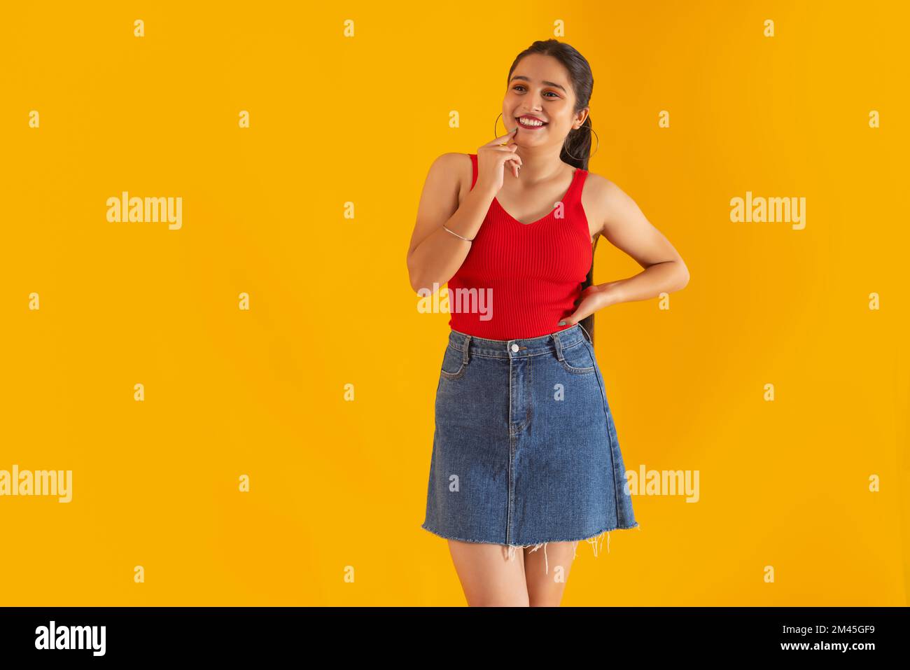 Ragazza giovane allegra guardando via con mano sul mento contro sfondo giallo Foto Stock