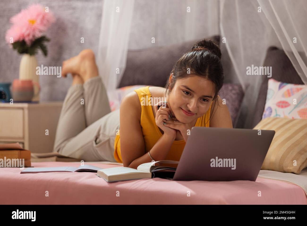Ragazza adolescente sdraiata a letto e studia con il laptop Foto Stock