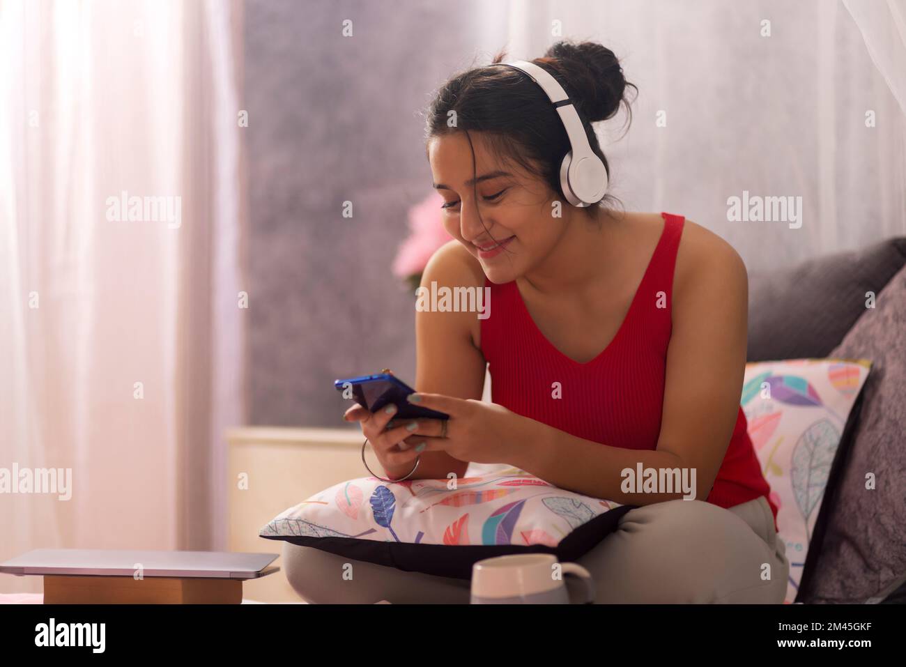 Ragazza adolescente che ascolta musica con le cuffie mentre si siede a letto Foto Stock