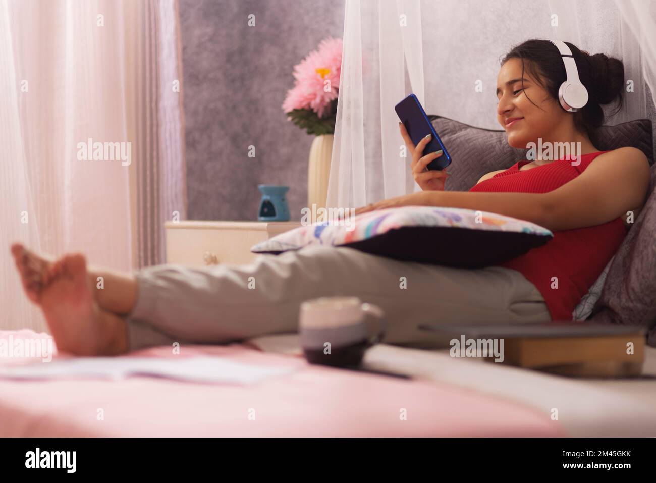 Ragazza adolescente che ascolta musica con le cuffie mentre si rilassa a letto Foto Stock