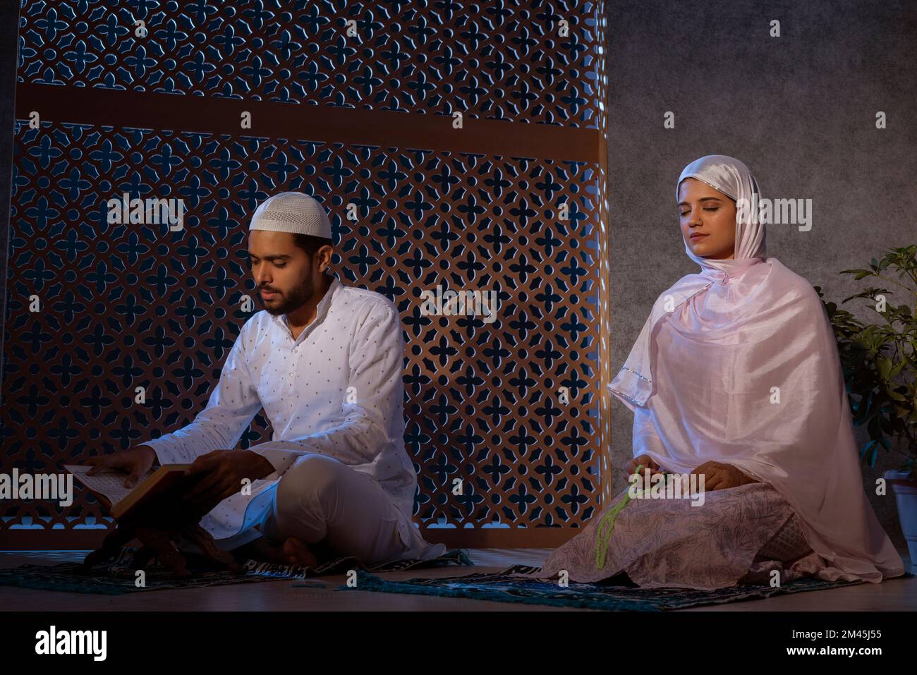 Uomo musulmano che legge il Corano e donna che prega con un perline di preghiera Foto Stock
