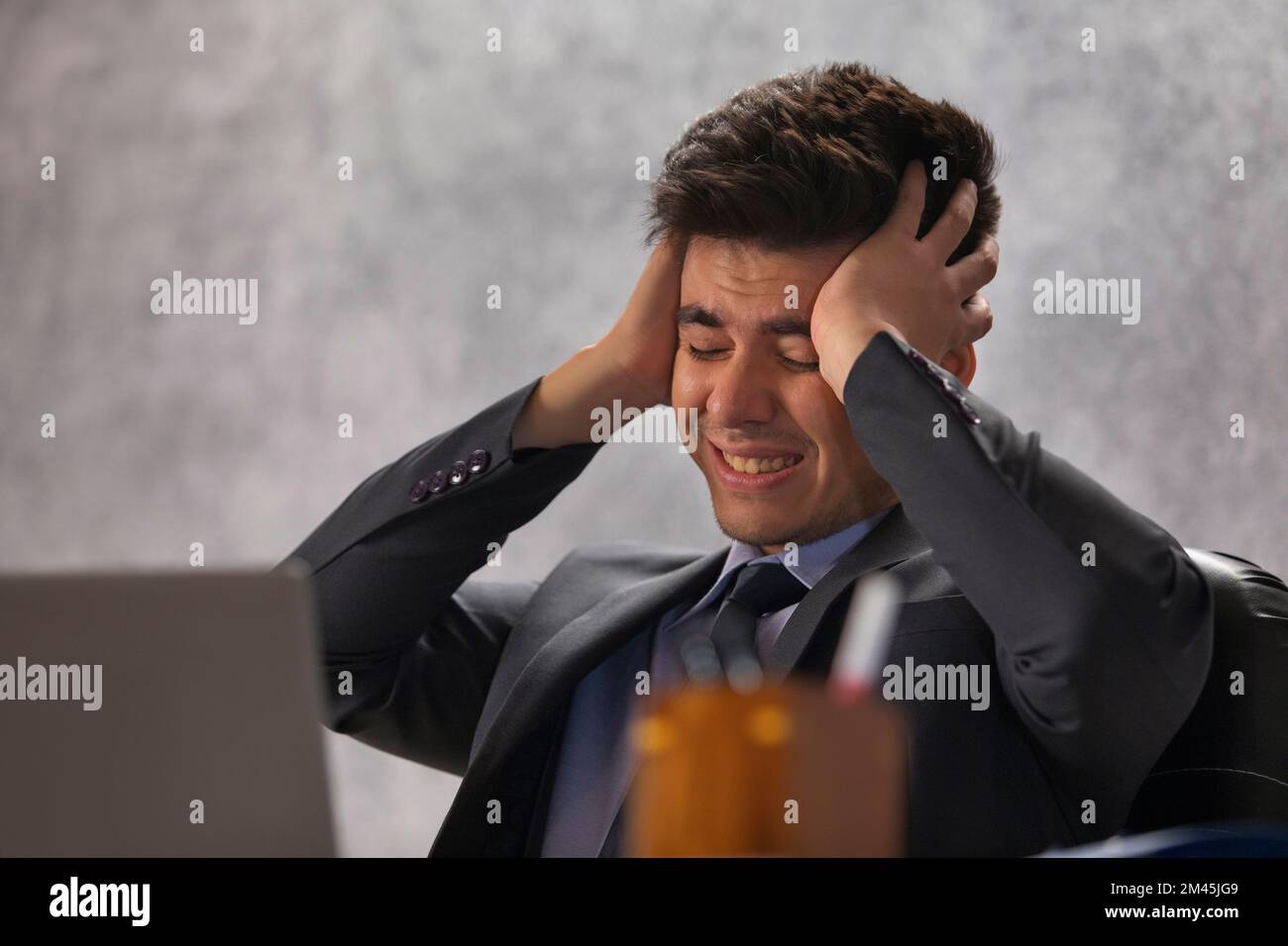 Ritratto di un giovane uomo d'affari stressato seduto alla sua scrivania con le mani sulla testa iin ufficio Foto Stock
