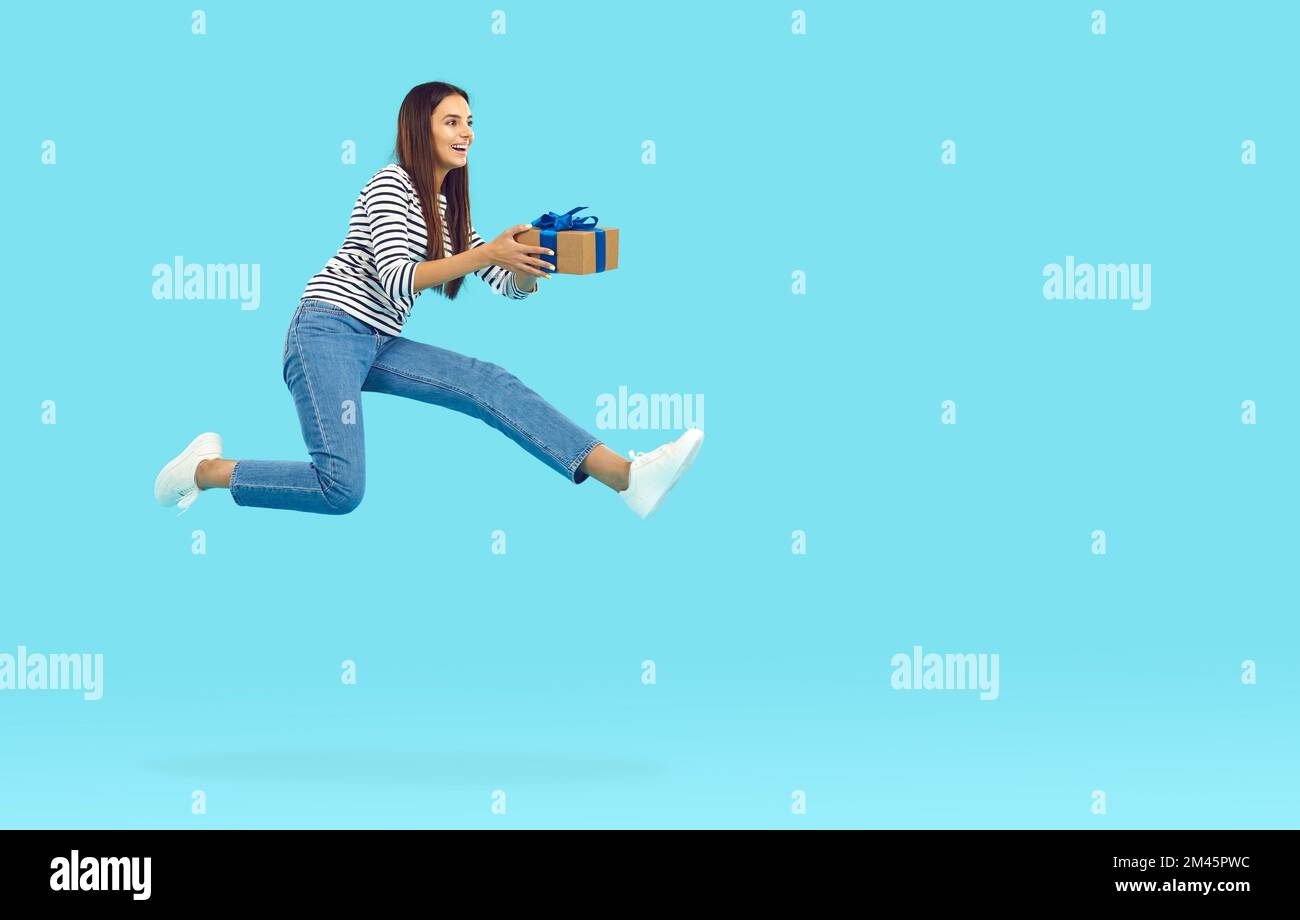 Felice donna gioiosa che tiene la scatola del regalo, saltando e volando sullo sfondo blu dello spazio della copia Foto Stock