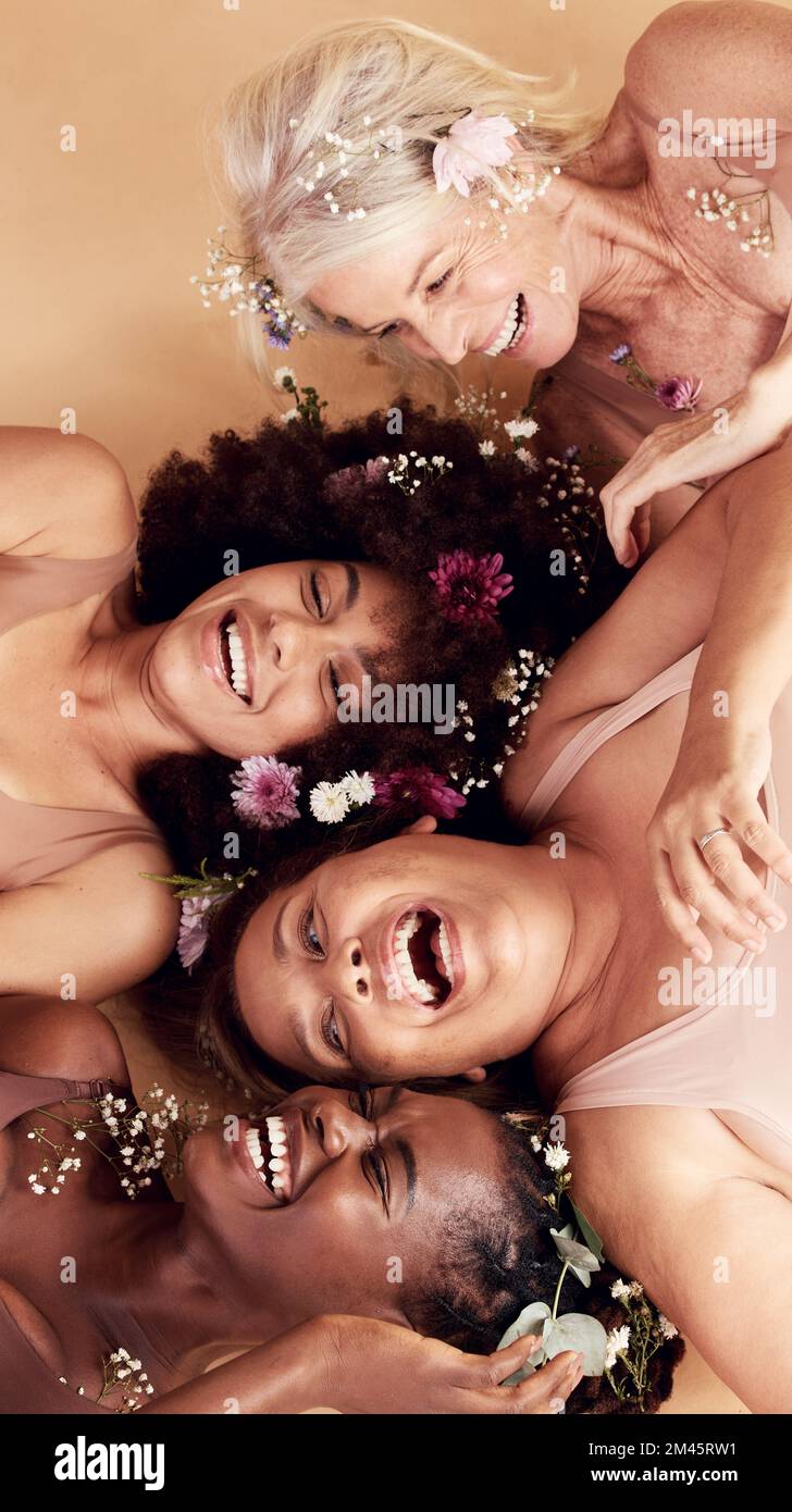 Vista dall'alto, diversità e donne con fiori, cosmetici e cura della pelle su uno sfondo marrone studio. Multirazziale, femmine e donne con positività corporea Foto Stock